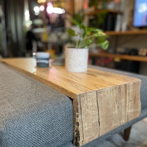 May include: A wooden tray with a natural wood finish sits on a grey sofa. The tray has a raised edge and is ideal for holding snacks or drinks.