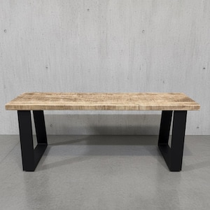 Peut inclure: Une table basse rectangulaire avec un dessus en bois clair et texturé et des pieds en métal noir. La table mesure environ 122 cm de long et 61 cm de large, avec un design moderne et minimaliste. Les pieds sont inclinés pour la stabilité.