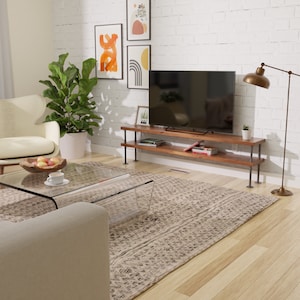 Puede incluir: Un soporte de TV de madera r&uacute;stica con patas de tuber&iacute;a met&aacute;lica. El soporte tiene dos estantes para almacenamiento y se muestra en un ambiente de sala de estar con un televisor, una alfombra y una mesa de caf&eacute;.