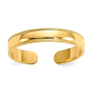 Puede incluir: Un anillo de dedo del pie de color dorado con una superficie pulida y reflectante. El anillo abierto presenta un diseño de cuentas a lo largo de los bordes y una banda lisa y curvada. El anillo está diseñado para ser usado en el dedo del pie.
