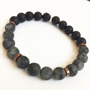 May include: A black and grey beaded bracelet with copper accents. The bracelet is made with lava rock and grey agate beads.