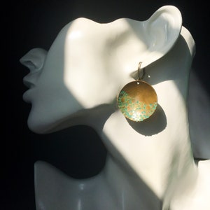 May include: A pair of round brass earrings with a turquoise blue enamel design. The earrings have a textured surface with small circles.