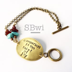 May include: A brass bracelet with a charm that reads "comparison is the thief of joy". The bracelet also features a turquoise stone and brown beads.