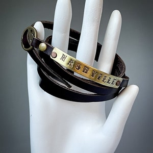 May include: A brown leather wrap bracelet with a brass plate engraved with the word "NASHVILLE".