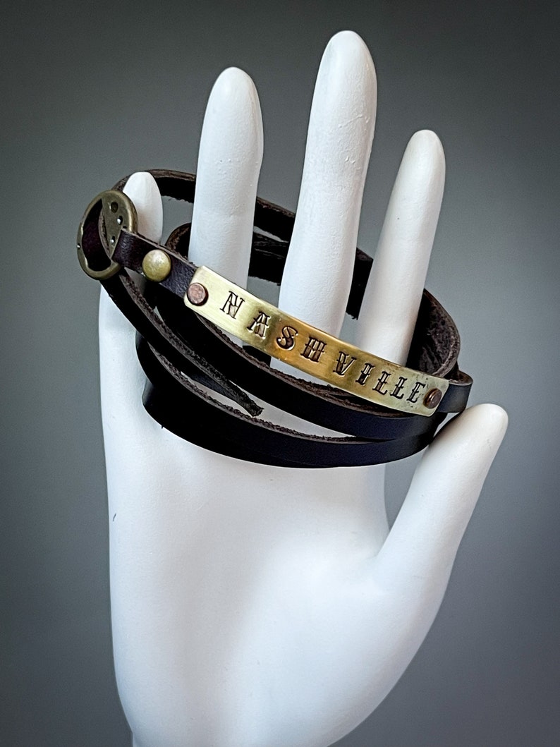 May include: A brown leather wrap bracelet with a brass plate engraved with the word "NASHVILLE".