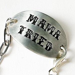 May include: A silver chain bracelet with a silver oval charm that says "Mama Tried" in black lettering.