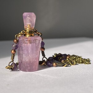 May include: A pink amethyst crystal bottle pendant necklace with a gold chain and purple beads.