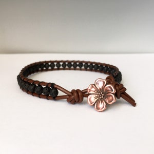 May include: A brown leather bracelet with black lava rock beads and a copper flower charm.