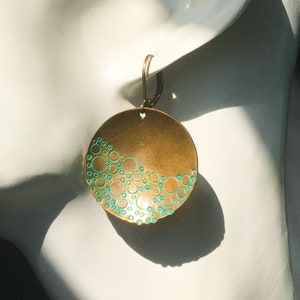 May include: Brass earrings with a teal blue enamel design of circles. The earrings are round and have a slightly curved shape.
