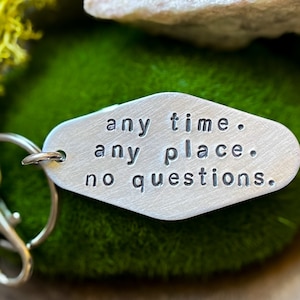 May include: Silver keychain with a diamond-shaped tag that reads "any time. any place. no questions."