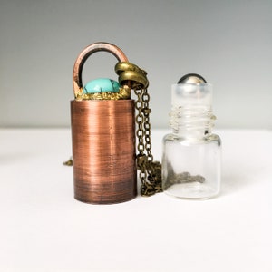May include: A copper and brass pendant necklace with a turquoise stone and a clear glass roller bottle. The necklace has a chain with a lobster clasp.