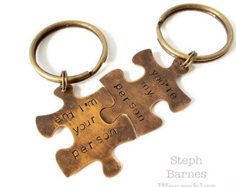 May include: Two interlocking bronze puzzle pieces with key rings. The left piece reads "and i'm your person" and the right piece reads "you're my person".