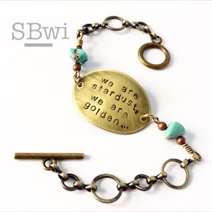 May include: A brass bracelet with a charm that reads "We are stardust, we are golden..." The bracelet also features turquoise and copper beads and a toggle clasp.