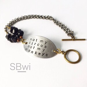 May include: A silver bracelet with a silver oval charm that says "not my circus not my monkeys". The bracelet has black beads and a brass clasp.
