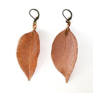 May include: A pair of copper leaf earrings with a textured surface and a wire hook closure.