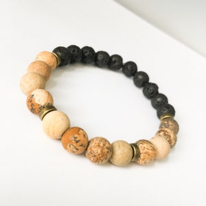 May include: A beaded bracelet with brown, beige, and black beads. The bracelet has a two-tone design with black lava beads on one half and brown and beige jasper beads on the other half.