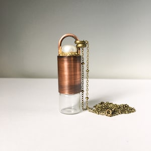 May include: A copper and glass pendant necklace with a pearl accent. The necklace has a chain made of brass.