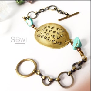 May include: A brass bracelet with a charm that reads "Not my circus, not my monkeys". The bracelet has turquoise and brown beads and a toggle clasp.