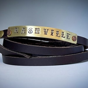 May include: A brown leather wrap bracelet with a gold metal plate engraved with the word "NASHVILLE".