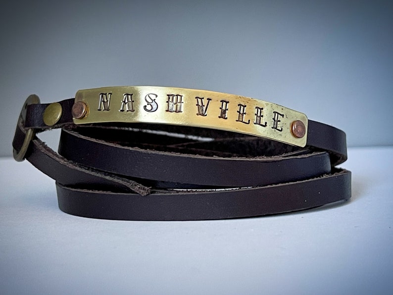 May include: A brown leather wrap bracelet with a gold metal plate engraved with the word "NASHVILLE".