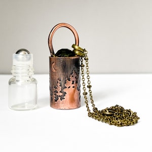 May include: A copper and brass necklace with a rollerball bottle pendant. The bottle has a moon and tree design. The necklace is 18 inches long.