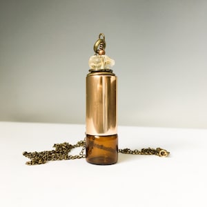 May include: A copper and glass essential oil diffuser necklace with a clear crystal charm. The necklace has a brown chain.