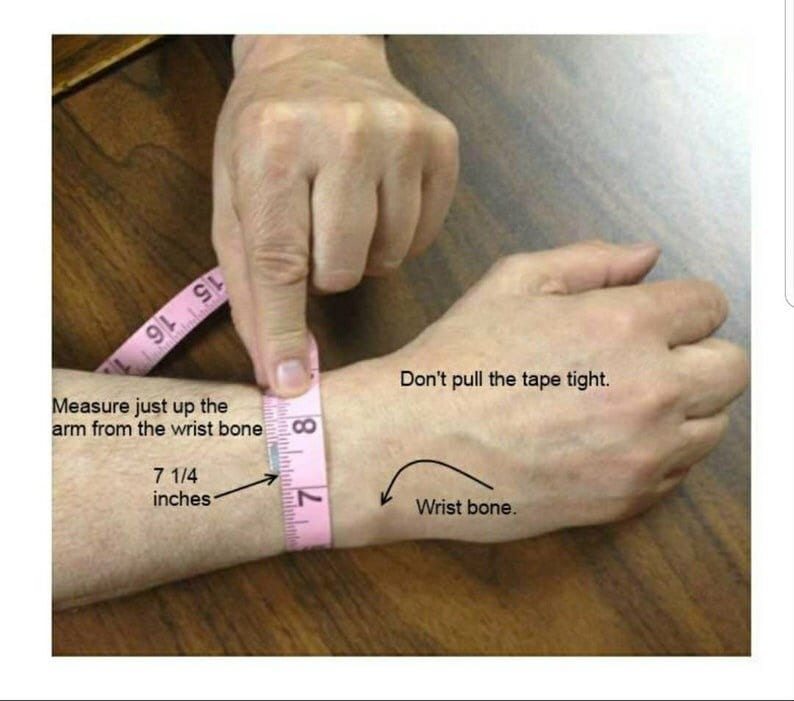 Op de afbeelding: Een roze meetlint is om de pols van een persoon gewikkeld om te laten zien hoe je voor een armband moet meten. De tekst op de afbeelding luidt "Meet gewoon omhoog langs de arm vanaf het polsbot 7 1/4 inch" en "Trek het lint niet te strak. Polsbot."
