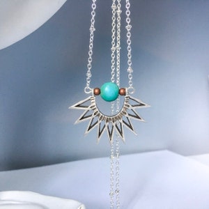 May include: A silver necklace with a turquoise stone pendant and a geometric sunburst design.