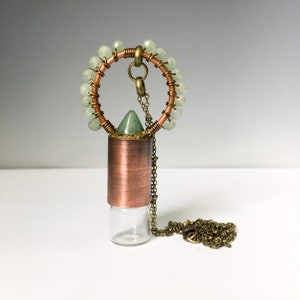 May include: A copper and glass essential oil diffuser necklace with a green stone pendant and a brass chain. The pendant is surrounded by a circle of green beads.