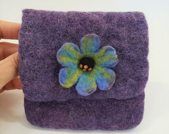 May include: A small, purple felted pouch with a flap closure. The pouch is decorated with a felt flower in shades of blue, green, and yellow, with an orange center. The pouch is handmade.