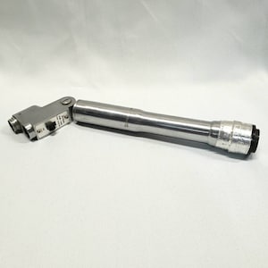 Puede incluir: Potencia de bicicleta plateada y ajustable, con cuerpo cilíndrico y cabezal rectangular. El cabezal tiene dos aberturas y texto. Diseñada para conectar el manillar a la horquilla de la bicicleta.