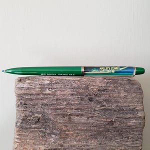 May include: A green pen with the text "M/S ROYAL VIKING SKY" and "HALLEY'S COMET 85-86". The pen has a silver band and a blue tip. The pen is resting on a piece of wood.
