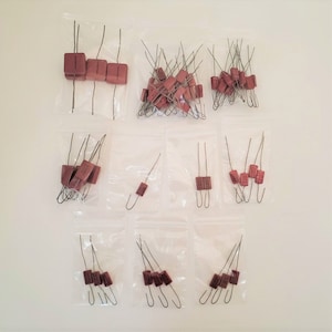 May include: A collection of vintage electronic components, including brown rectangular capacitors with wire leads, packaged in clear plastic bags. The components are arranged on a white background.
