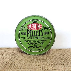 May include: A round, green tin of Keenfire .177 caliber pellets. The tin has a white and red logo with the word "PELLETS" in large letters. Text on the tin indicates it is for airguns and pistols, made in Japan.