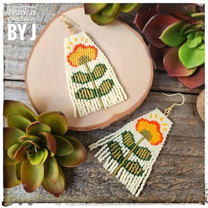 May include: Handmade beaded earrings with a floral design. The earrings feature a cream-colored base with a yellow and orange flower, green leaves, and a fringe. The text "Fearless Creations BY J" is in the upper left corner.