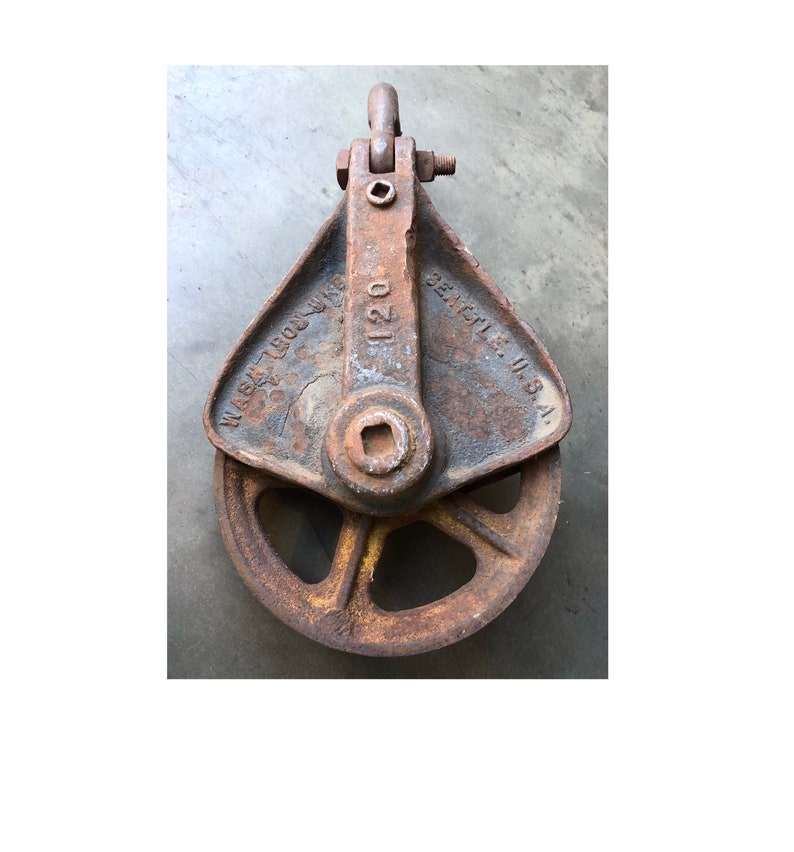 May include: A rusty metal pulley with a wheel and a hook. The pulley is labeled "SEATTLE, U.S.A." and "120".
