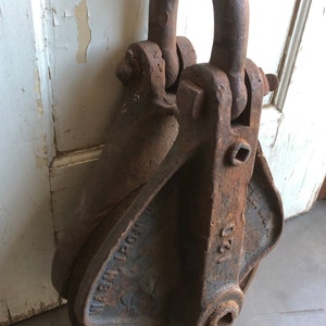 May include: A rusty metal pulley with a large, round wheel and a hook on top. The pulley is labeled "WABASH IRON WKS" and "U.S.A."