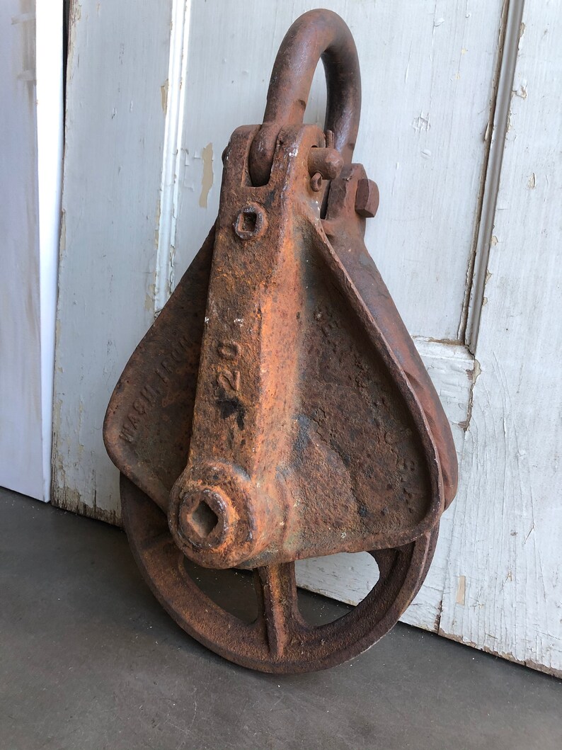 May include: A rusty metal pulley with a square hole in the center and a hook on top. The pulley has the text "MACHINERY" and "220" on the side.