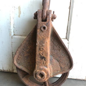 May include: A rusty cast iron pulley with a large wheel and a hook on top. The pulley is labeled "Wash Iron 200"