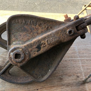 May include: A rusty cast iron pulley with a wheel and a hook. The pulley is labeled "WASH. IRON WKS" and "200".