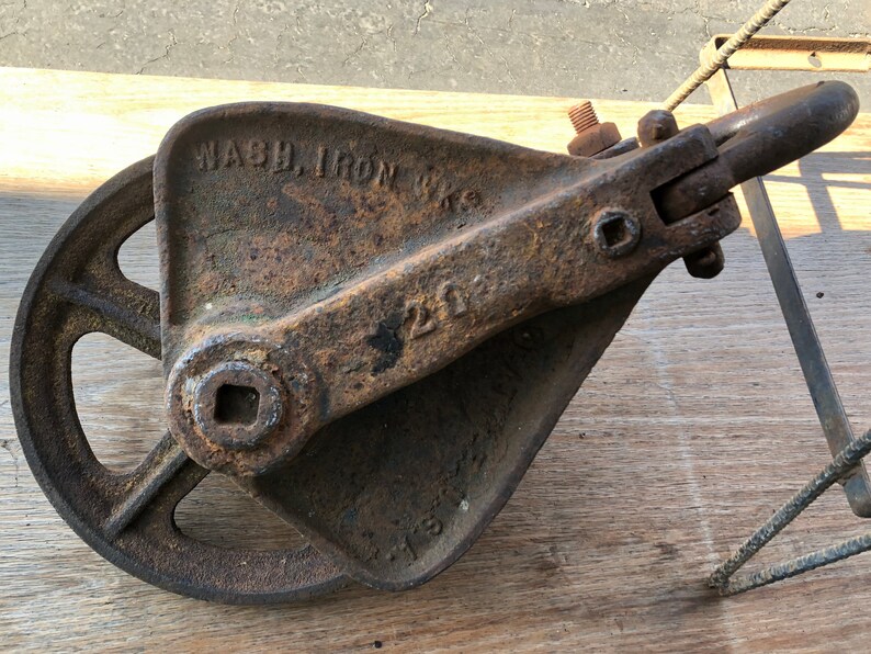 May include: A rusty cast iron pulley with a wheel and a hook. The pulley is labeled "WASH. IRON WKS" and "200".