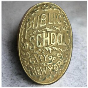 May include: An oval-shaped brass badge featuring raised lettering that reads PUBLIC SCHOOL CITY OF NEW YORK. The metal surface has a weathered, aged patina with intricate decorative scrollwork patterns surrounding the embossed text.