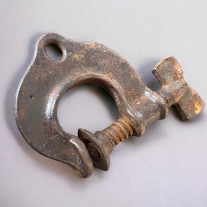 May include: A rusty metal clamp with a screw and a handle. The clamp is used to hold objects together.