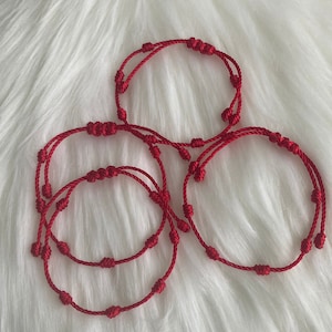 May include: Three red string bracelets with knots. The bracelets are made of a thin, red cord and have a simple, elegant design.