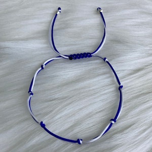 May include: A blue and white friendship bracelet with silver beads. The bracelet is made of two strands of cord, one blue and one white, that are tied together with knots.