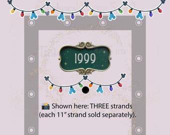 May include: A decorative sign featuring the number 1999 in a dark green frame, accompanied by two strands of colorful light bulbs with Mickey Mouse ear shapes. Text states: Shown here: THREE strands (each 11" strand sold separately).