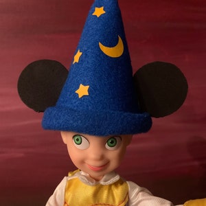 May include: A blue felt sorcerer's hat with yellow stars and a crescent moon design. The hat has black Mickey Mouse ears attached to the sides.