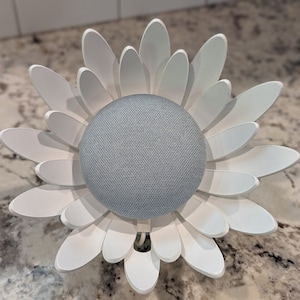 May include: A white daisy-shaped stand with a gray smart speaker in the center. The stand is made of plastic and has a smooth finish.