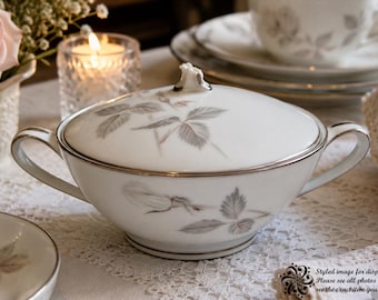 May include: A white porcelain sugar bowl with a lid, featuring a delicate grey rose and leaf pattern and silver trim. The bowl has two side handles and a small decorative finial on the lid. The text on the image reads: Styled image for display purposes only. Please see all photos in the listing to see the exact item you will receive.
