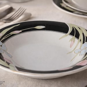 May include: White ceramic bowl with a black rim, decorated with floral designs in light blue, pink, and green. The bowl is part of a dinnerware set, with a matching plate visible in the background.